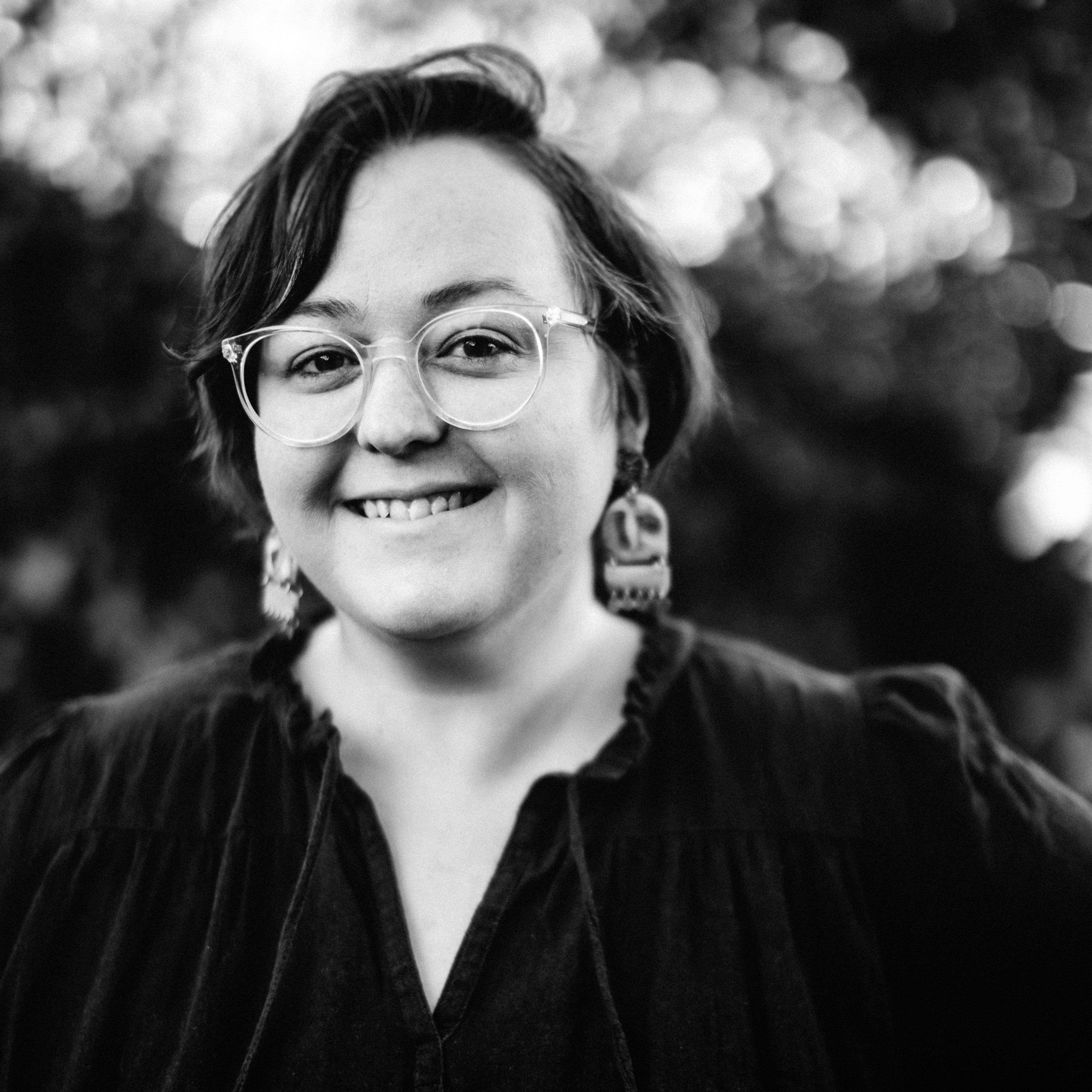 Black and white portrait of a person with glasses and earrings outdoors.